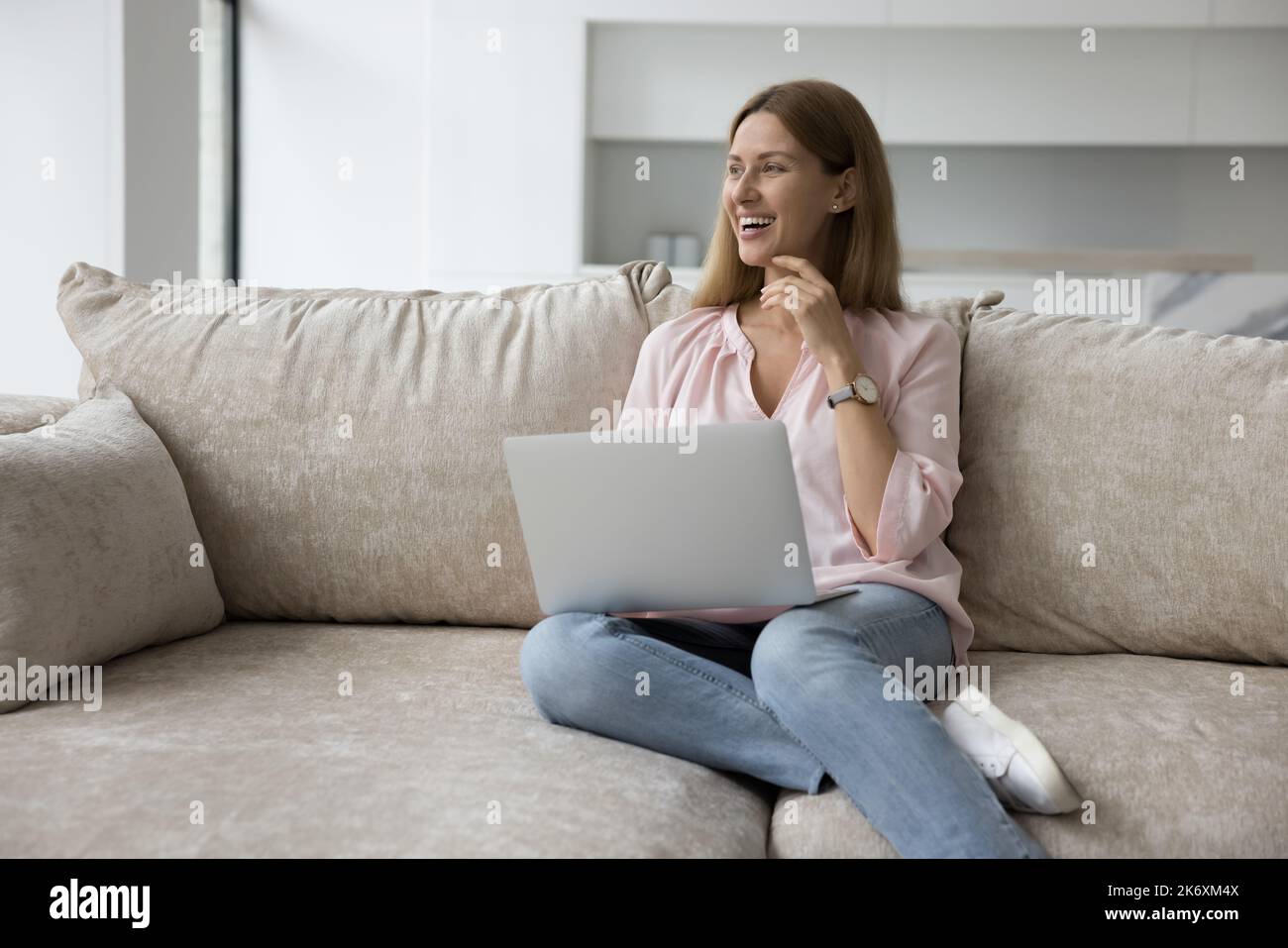 Une femme rêveuse qui se tient à distance pour se détendre sur un canapé avec un ordinateur portable Banque D'Images