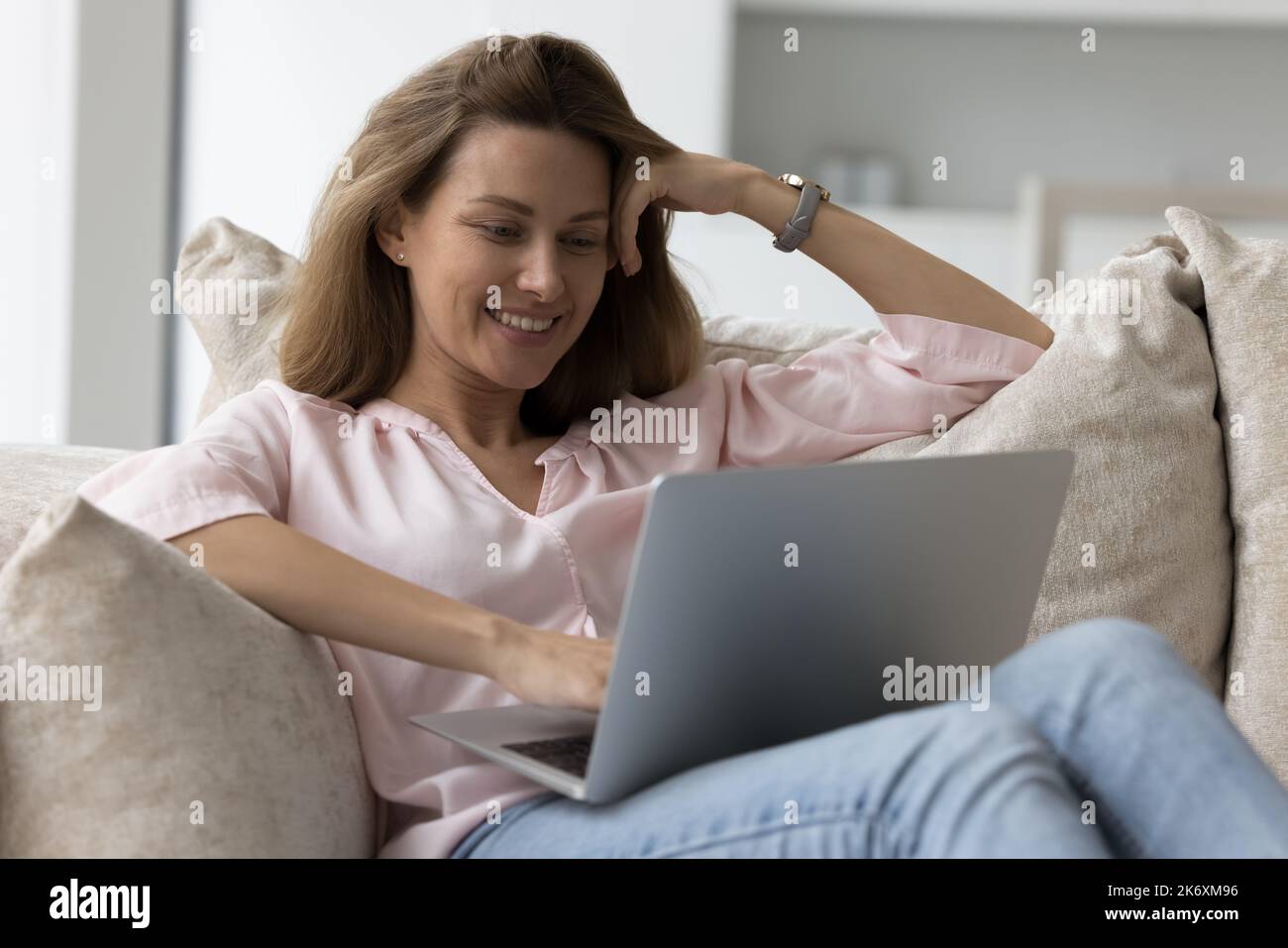 Une femme attirante se détend sur des coussins confortables avec un ordinateur portable Banque D'Images