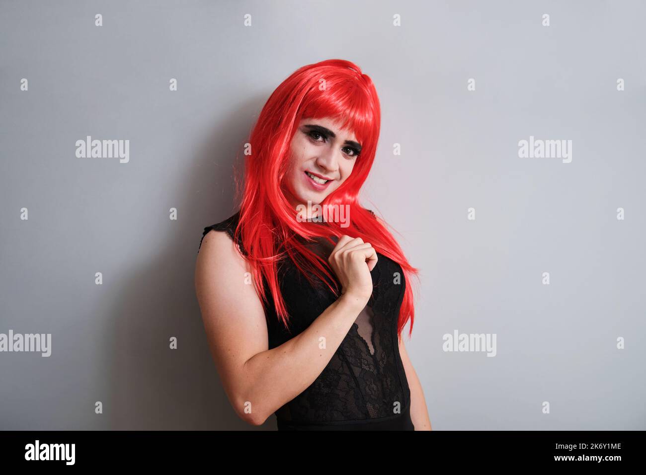 Portrait d'une reine de drag souriant portant une perruque rouge sur fond gris. Banque D'Images