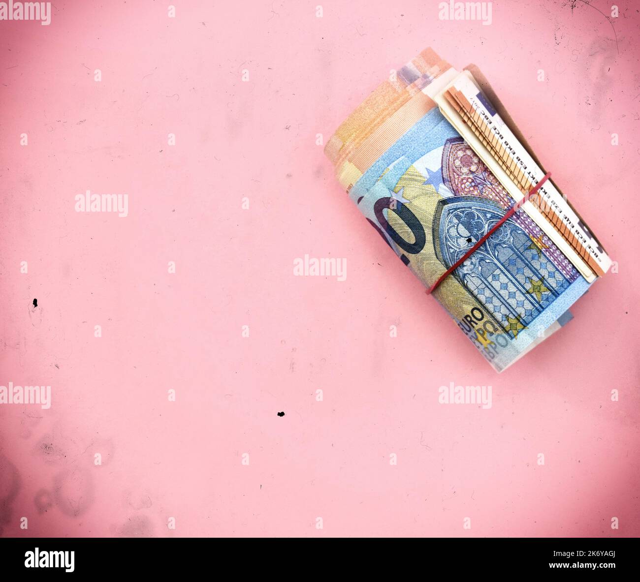Rouleau de 20 billets en euros (avec 50 et 100 euros à l'intérieur) avec bande en caoutchouc rouge. Argent/finance sur fond rose Banque D'Images
