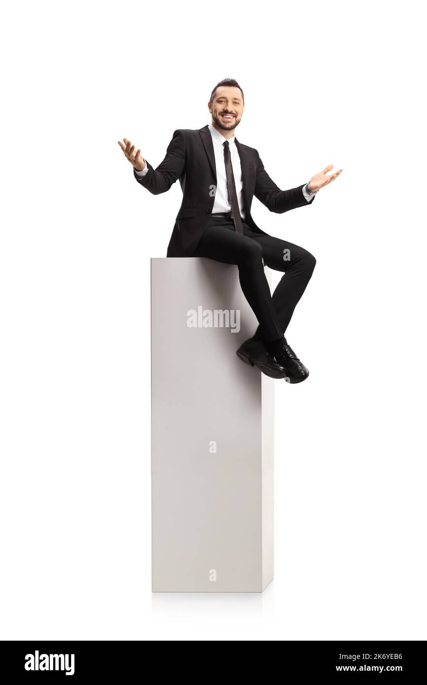 Homme d'affaires gai assis sur une grande colonne blanche et souriant à l'appareil photo isolé sur fond blanc Banque D'Images