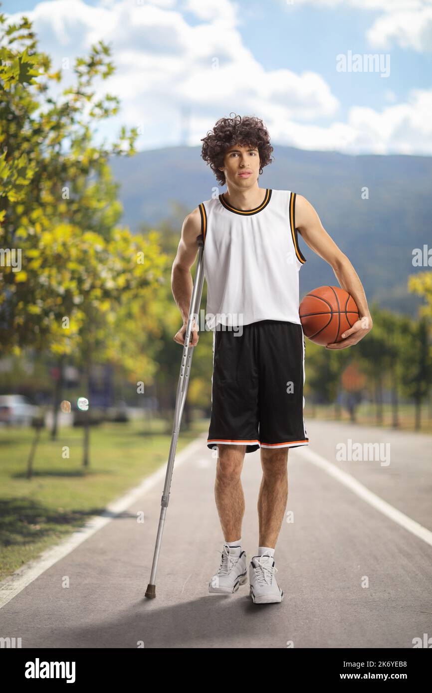 Joueur de basket-ball tenant une balle et marchant avec une béquille sur un chemin piétonnier Banque D'Images