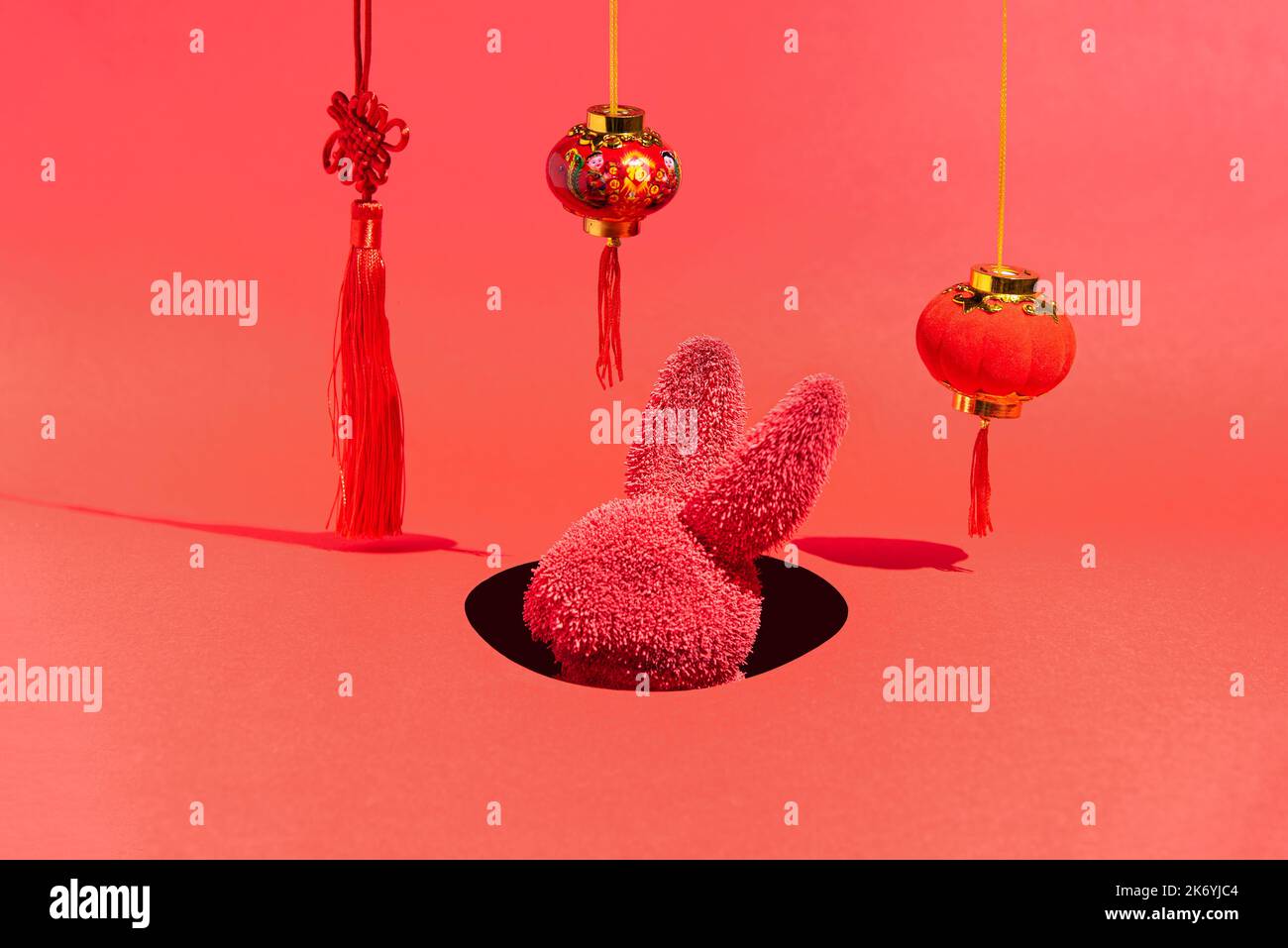 Un lapin rouge dans un trou entouré de décorations du nouvel an sur un fond rouge. Lapin chinois nouvel an. Présentation isométrique. Concept abstrait minimal. Banque D'Images