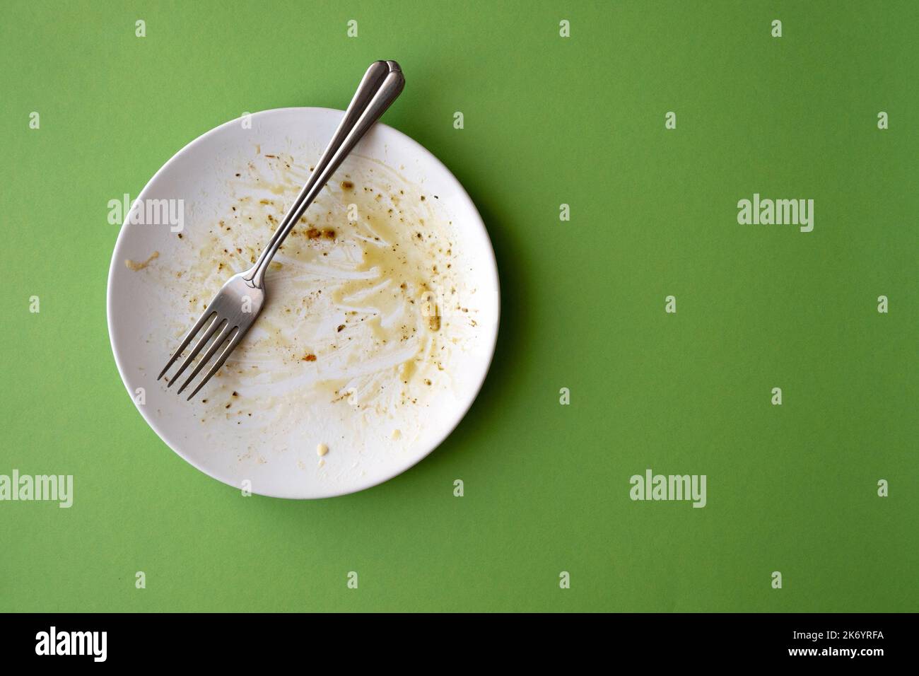 Assiette en céramique blanche avec restes de nourriture, pâtes, huile d'olive, sauce et fourchette sur fond vert. Image créative avec espace pour le texte Banque D'Images