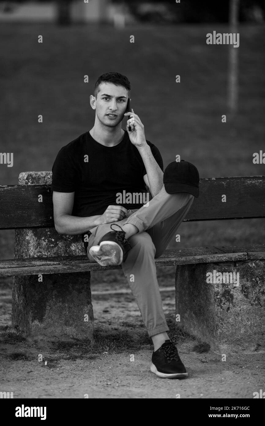 Beau jeune homme assis sur un banc parlant sur son téléphone. Photo en noir et blanc. Banque D'Images