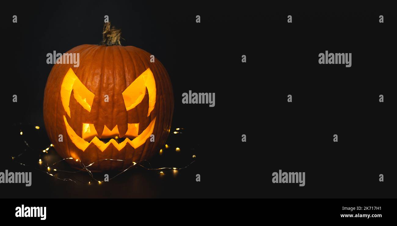 Véritable citrouille orange d'Halloween sur fond noir avec des lumières fée donnant des vibes effrayantes de saison. Portrait de la tête de citrouille effrayant illuminant à l'intérieur avec de l'orange Banque D'Images