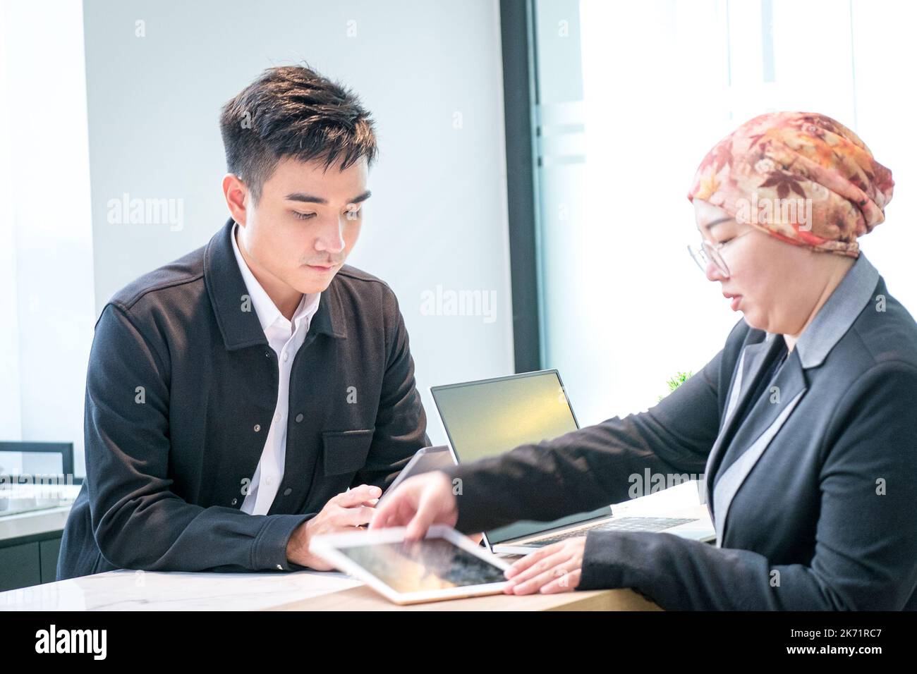 Deux hommes d'affaires asiatiques travaillent ensemble, regardant les tablettes au bureau. Banque D'Images
