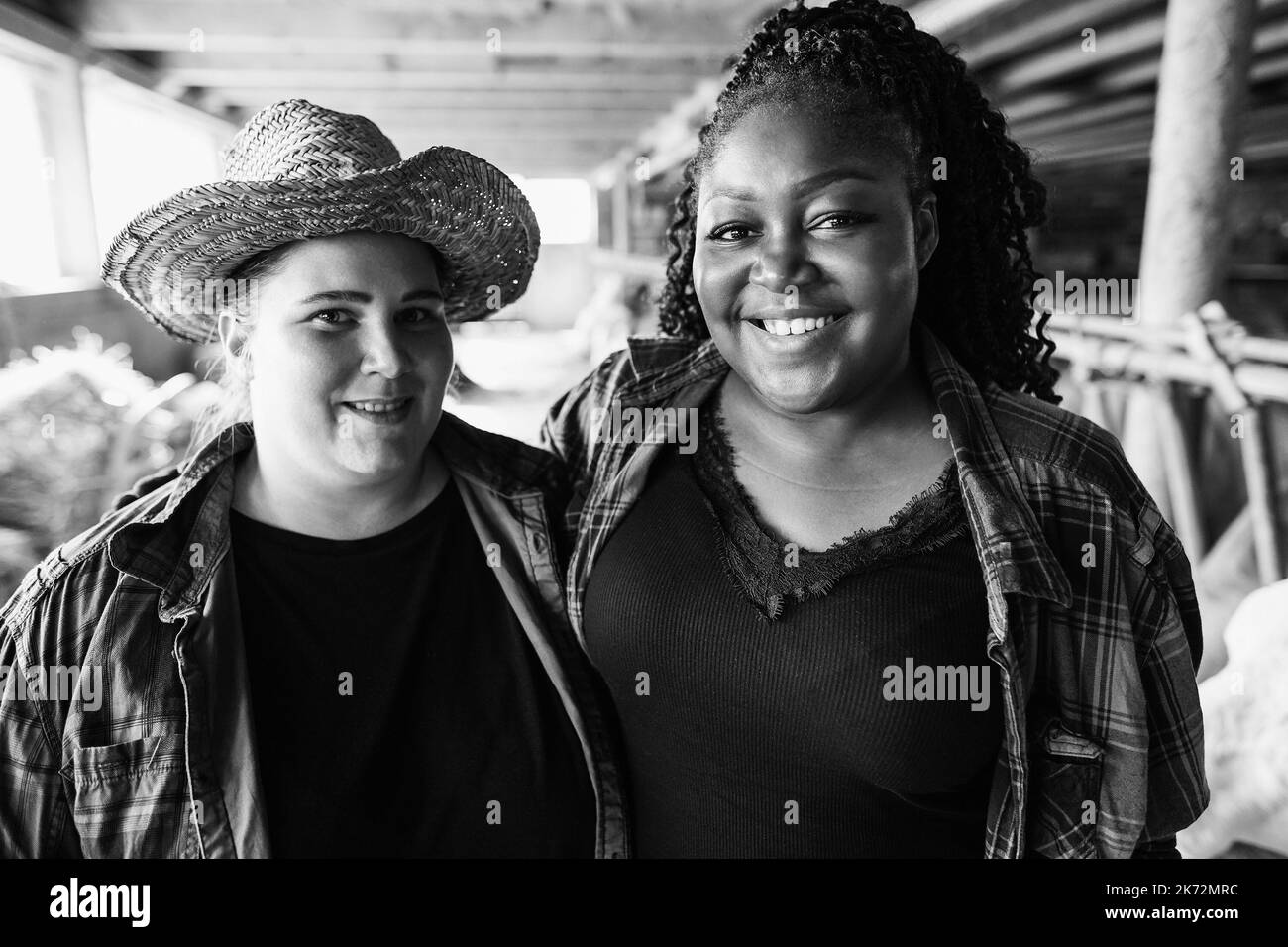 Jeunes agriculteurs multiraciaux travaillant à l'intérieur de Cowshed - Focus sur le visage des filles africaines - montage noir et blanc Banque D'Images