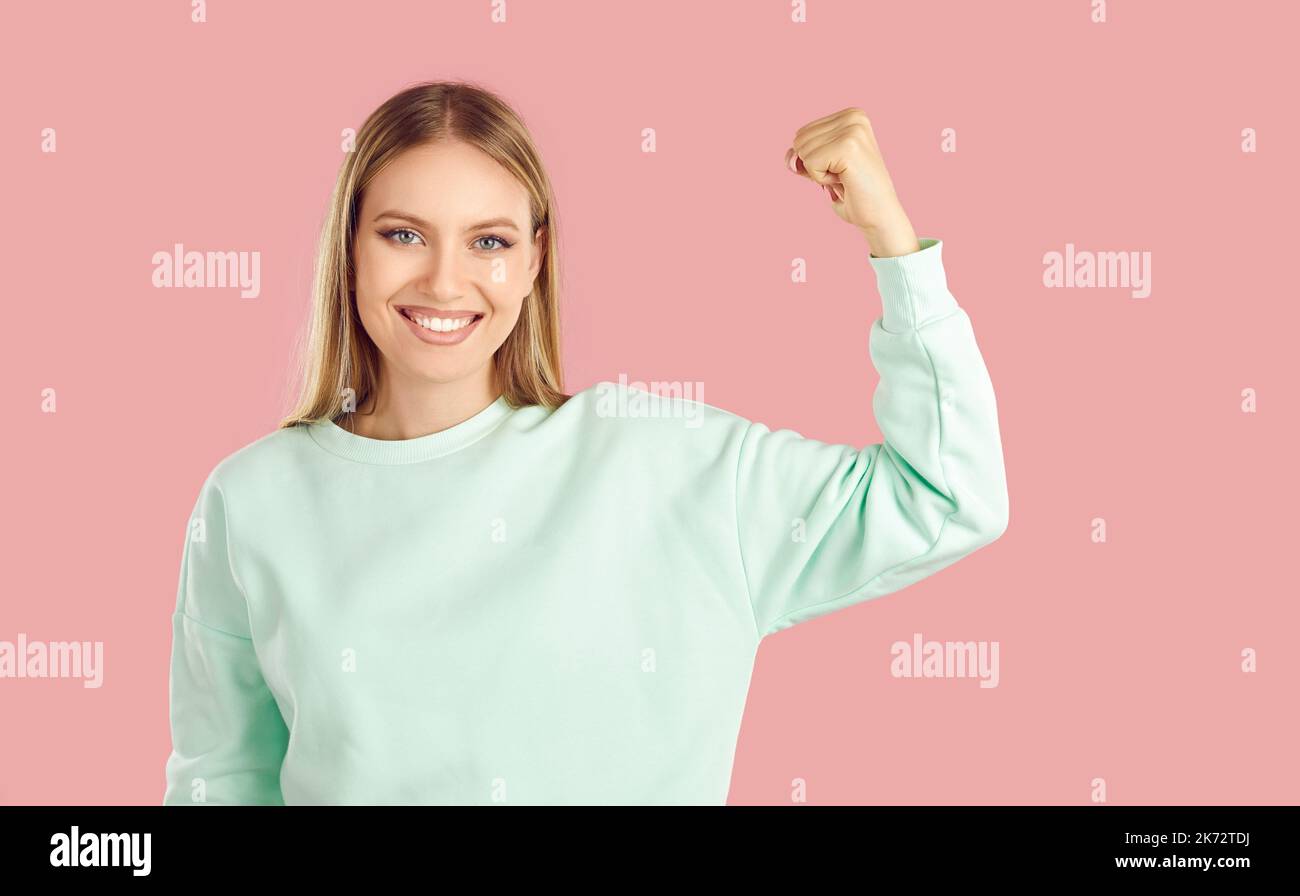 Belle femme souriante lève sa main montrant son biceps comme signe de sa force et de sa confiance. Banque D'Images