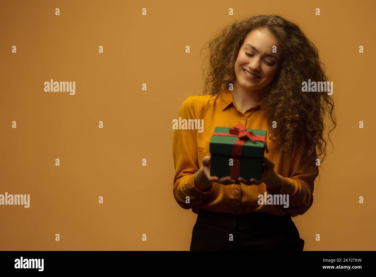 Portrait d'une jeune femme heureuse tenant une boîte cadeau, fond orange. Banque D'Images