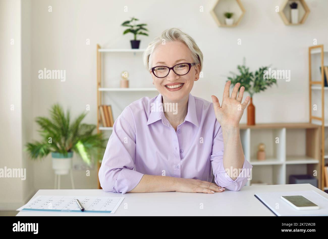 Bonne femme mûre commençant la conférence en ligne, regardant la caméra, en signe de bonjour et de sourire Banque D'Images