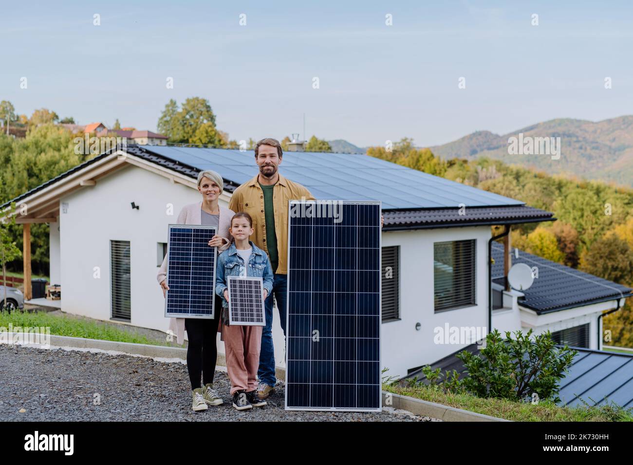 Famille heureuse près de leur maison avec panneaux solaires. Énergies alternatives, économies de ressources et concept de mode de vie durable. Banque D'Images