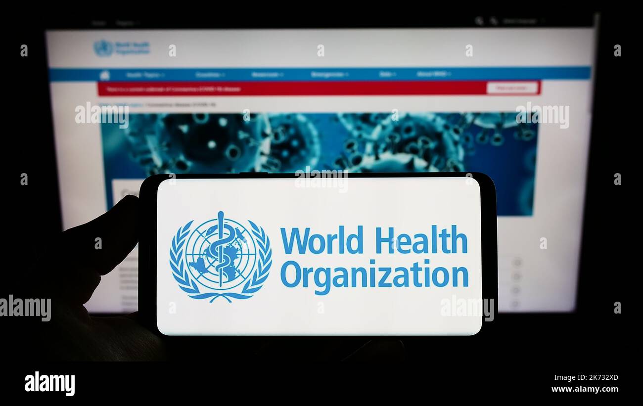 Personne tenant un smartphone avec le logo de l'Organisation mondiale de la Santé (OMS) de l'agence des Nations Unies sur l'écran devant le site Web. Mise au point sur l'affichage du téléphone. Banque D'Images