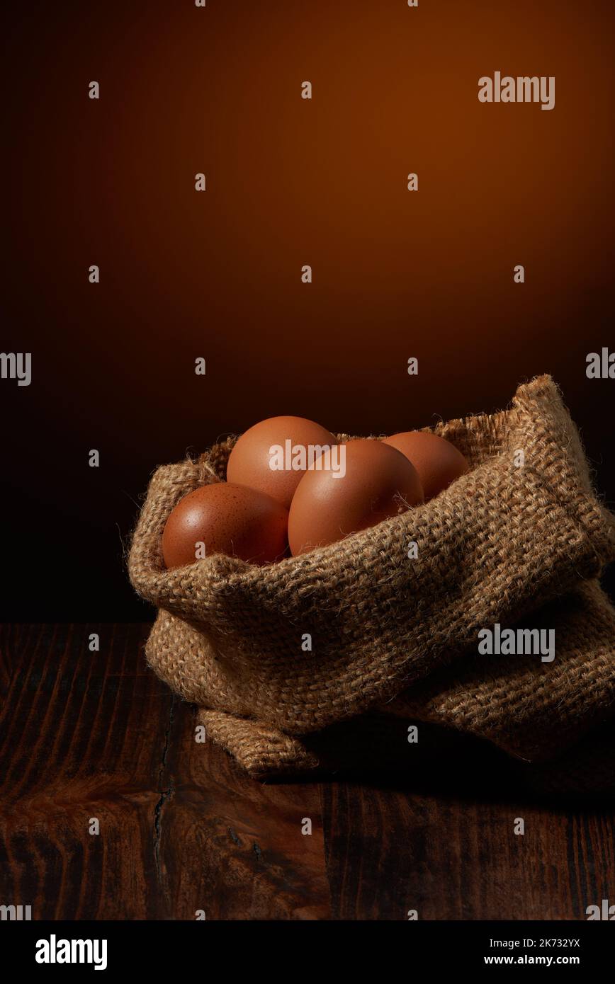 Faire dorer les œufs de poulet dans un sac de toile de jute sur une table en bois sombre et sur un fond rustique et chaleureux Banque D'Images