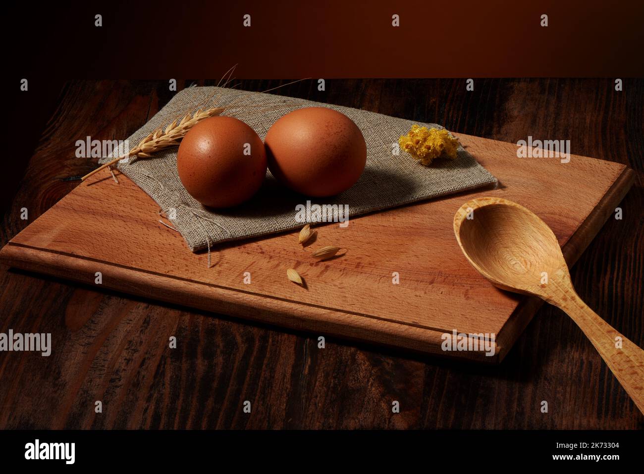 Deux œufs de poulet bruns sur une serviette en toile de jute et une cuillère en bois sur une table sombre et un fond rustique chaud Banque D'Images