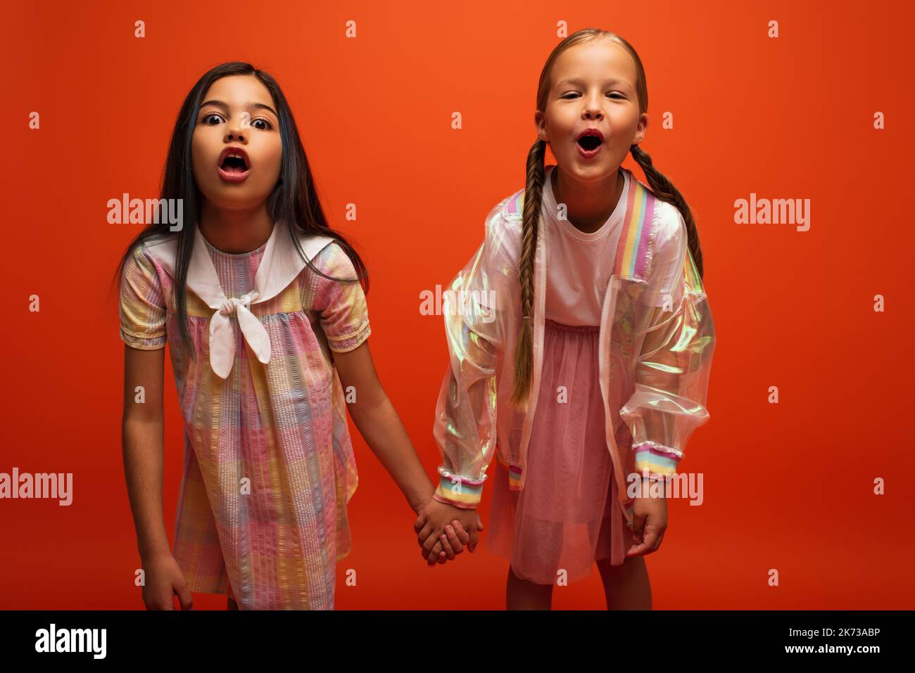 drôles filles avec des bouches ouvertes tenant les mains et grimacing à la caméra isolée sur l'orange Banque D'Images