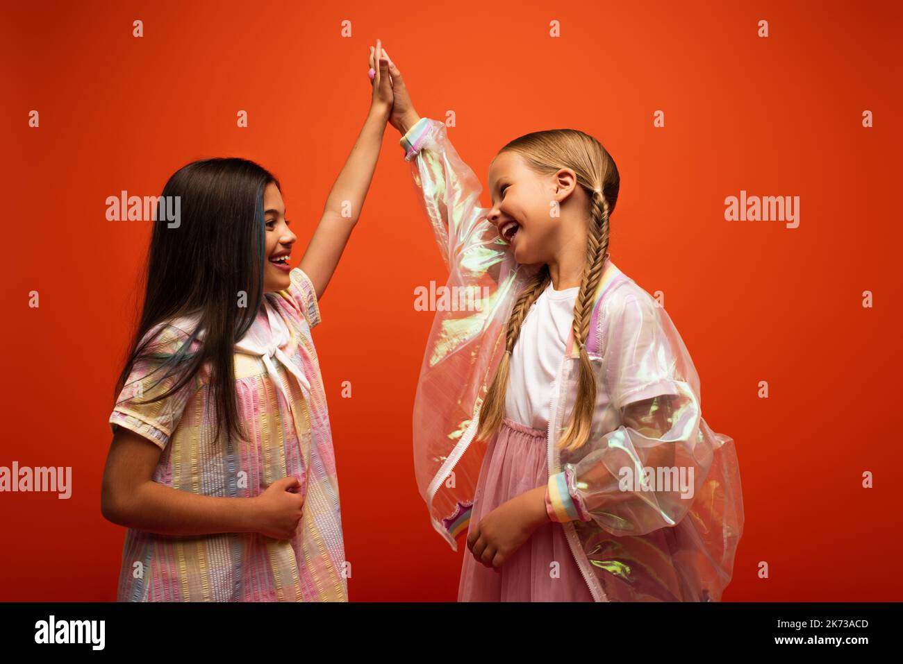 joyeuses filles en robe et veste de pluie transparente donnant haut cinq isolé sur orange Banque D'Images