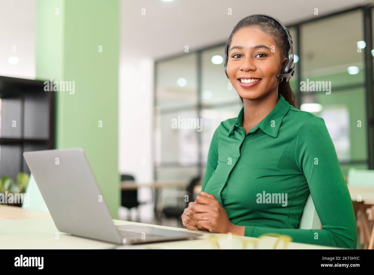 Prise de vue d'une jeune femme afro-américaine portant un casque sans fil, regardant la caméra avec le sourire. Femme gaie dans un casque avec micro, employé de service d'assistance au bureau Banque D'Images