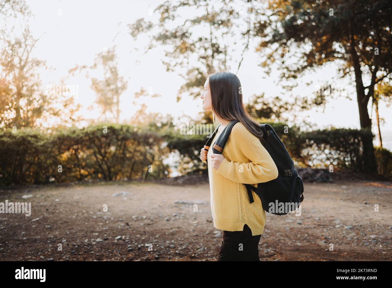 Vue latérale une étudiante de l'université portant un chandail jaune et un sac à dos dans la route du parc du campus. Sourire innocent Banque D'Images