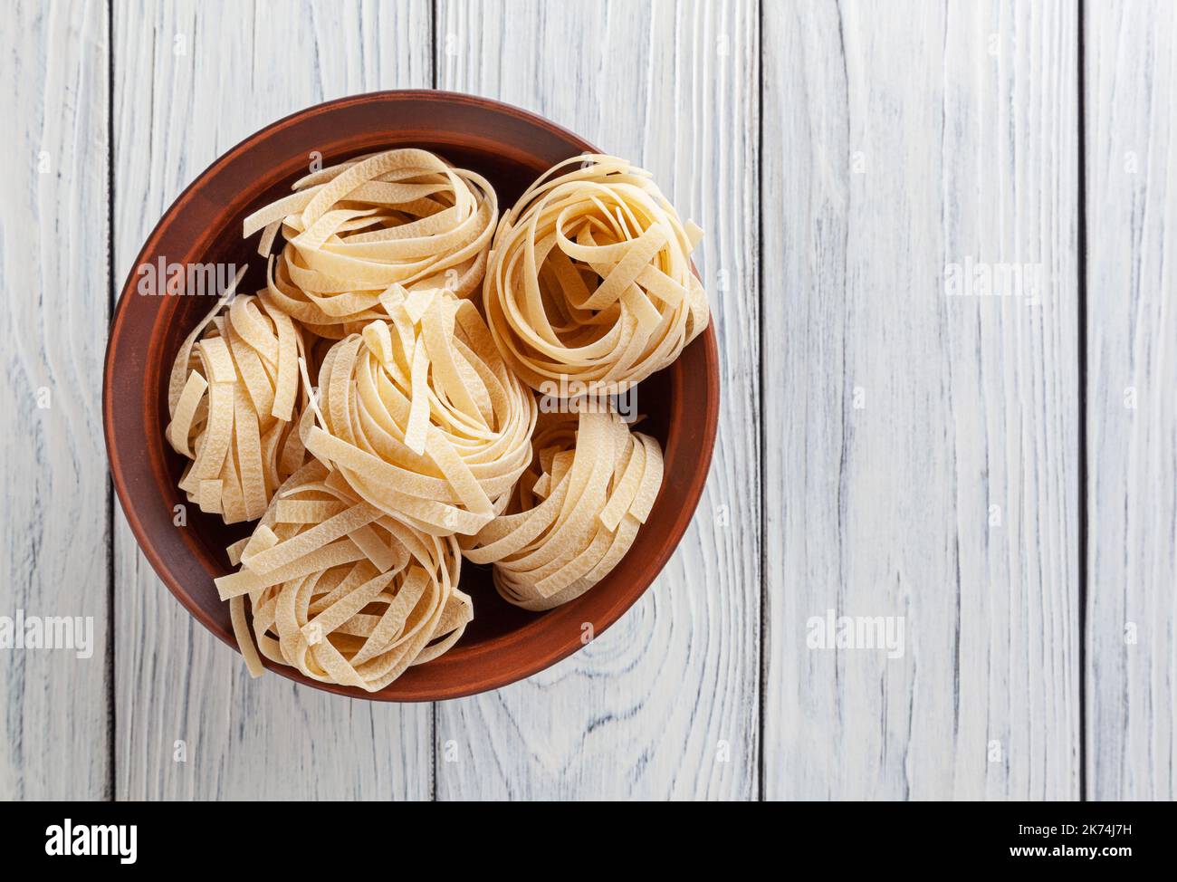 Pâtes tagliatelles non cuites dans un bol en céramique sur fond de bois blanc Banque D'Images