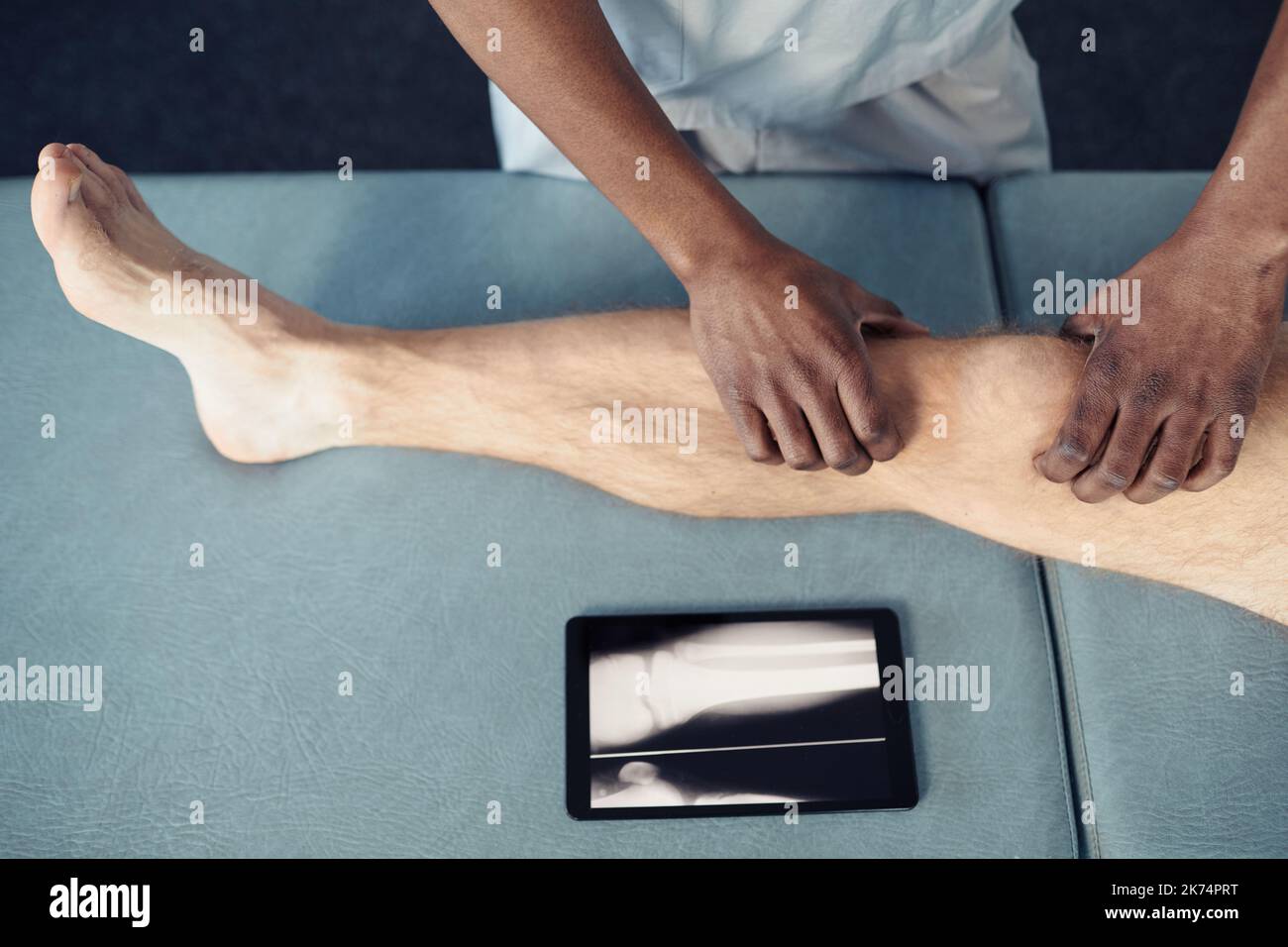 Vue en grand angle du thérapeute effectuant un massage médical au patient sur le canapé à l'aide d'une tablette numérique Banque D'Images