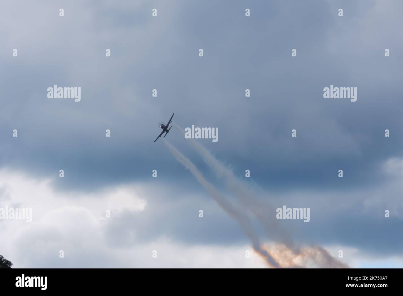 Avion grimpant avec de la fumée à l'arrière dans les nuages sombres Banque D'Images