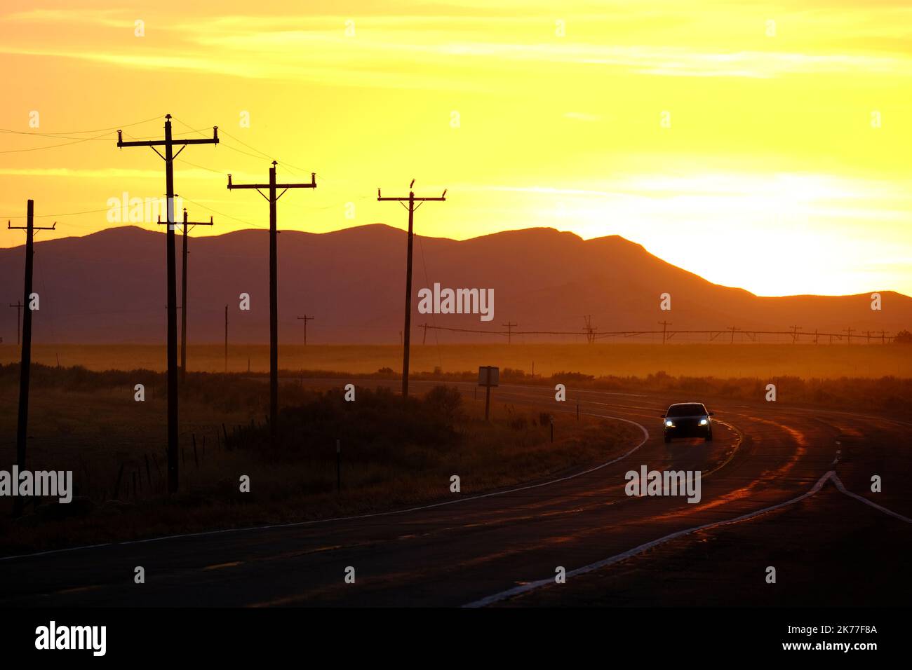 Voiture roulant sur la route au coucher du soleil ou au lever du soleil avec la silhouette des pôles de puissance Banque D'Images