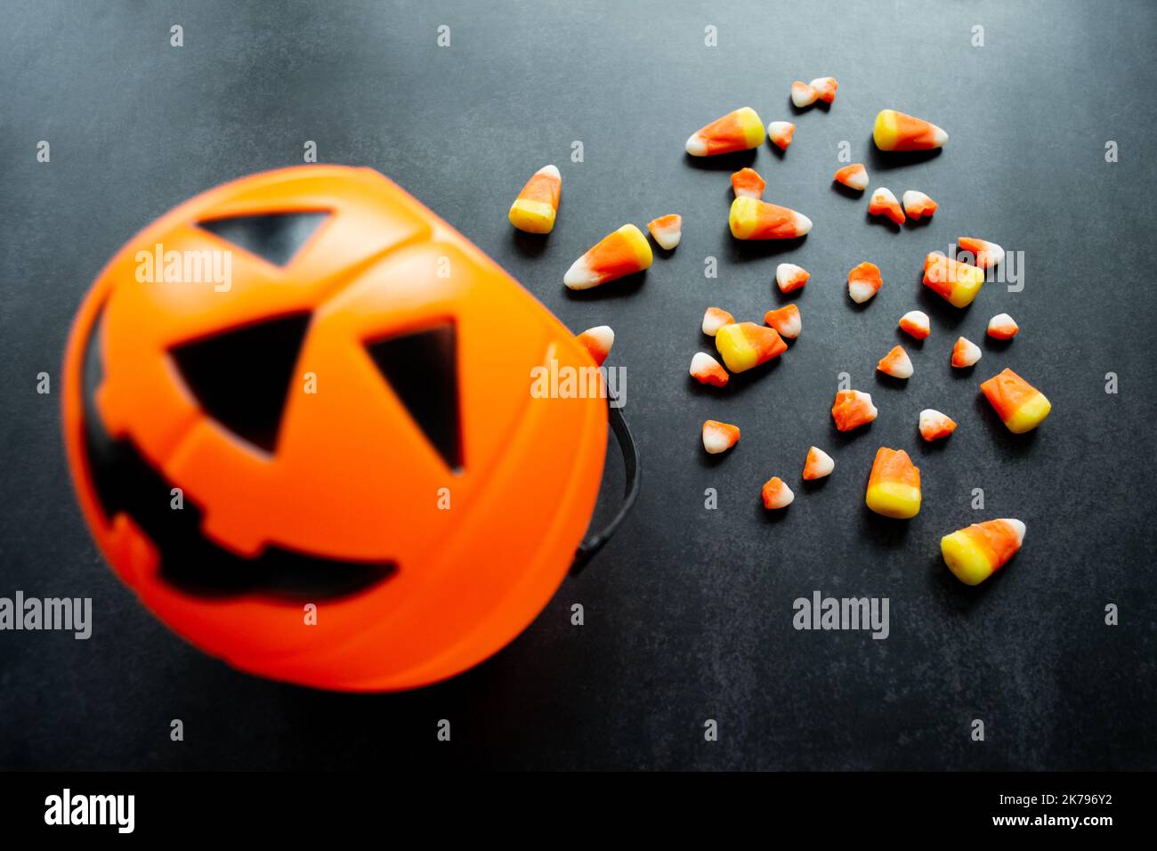 Panier de citrouille en plastique avec du maïs bonbon renversé. Certaines sont cassées et ressemblent à de petites dents. Halloween Nocif bonbons concept. Copier l'espace. Banque D'Images