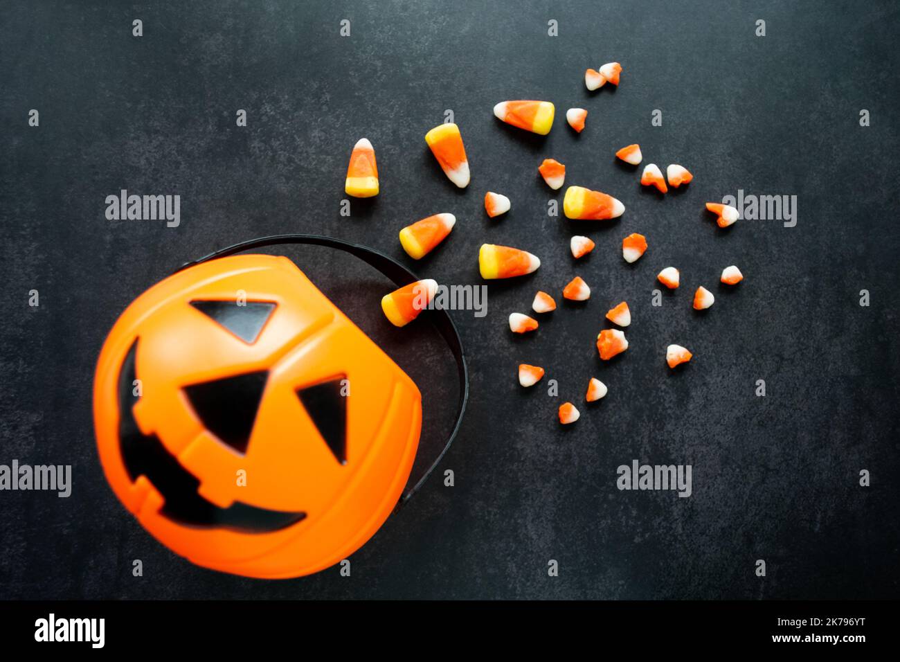 Panier de citrouille en plastique avec du maïs bonbon renversé. Certaines sont cassées et ressemblent à de petites dents. Halloween Nocif bonbons concept. Copier l'espace. Banque D'Images