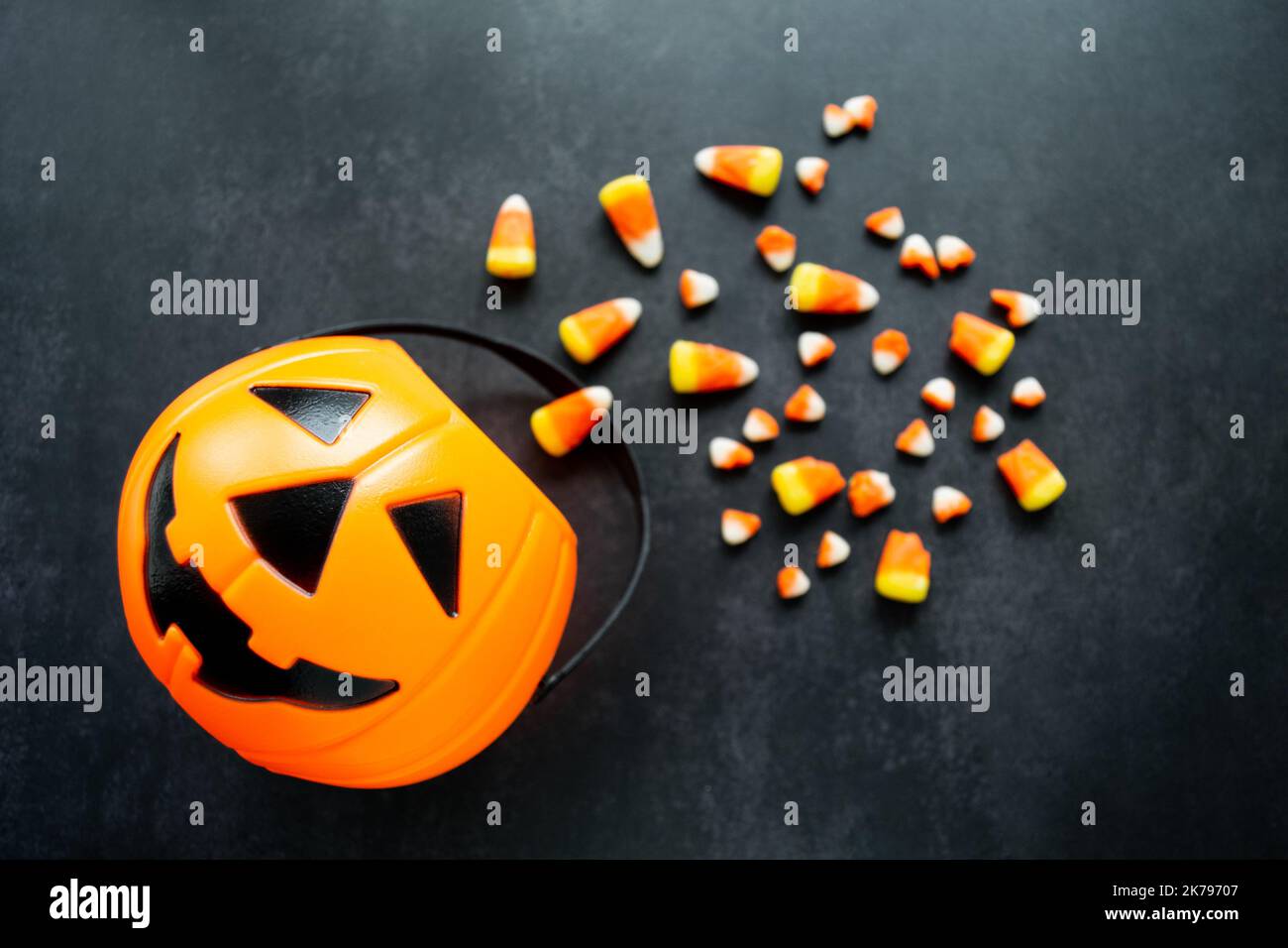 Panier de citrouille en plastique avec du maïs bonbon renversé. Certaines sont cassées et ressemblent à de petites dents. Halloween Nocif bonbons concept. Copier l'espace. Banque D'Images