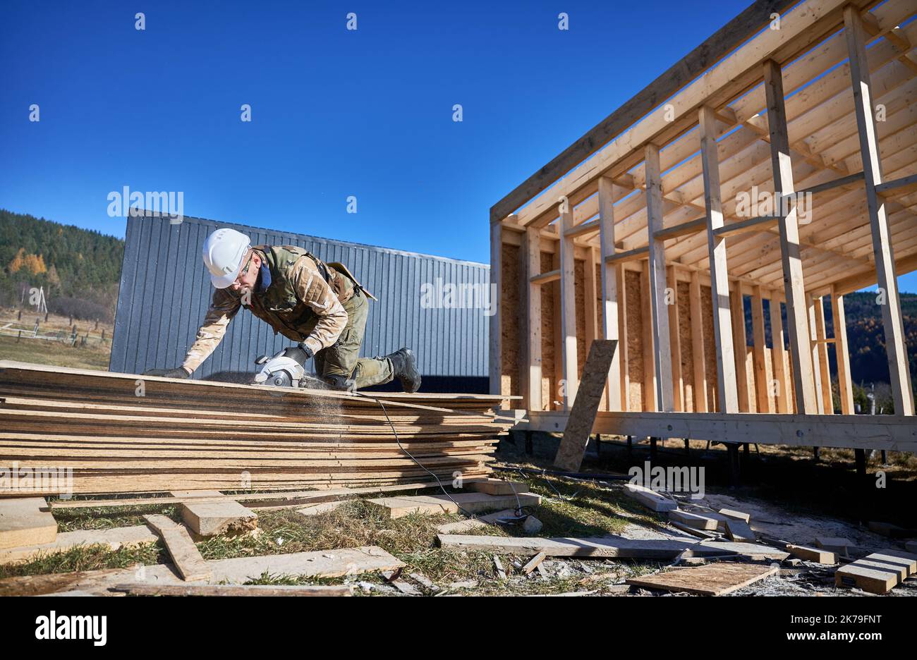 Menuisier utilisant une scie circulaire pour couper des panneaux OSB en bois. Homme ouvrier bâtiment maison de cadre en bois sur la base de pile. Concept de menuiserie. Banque D'Images