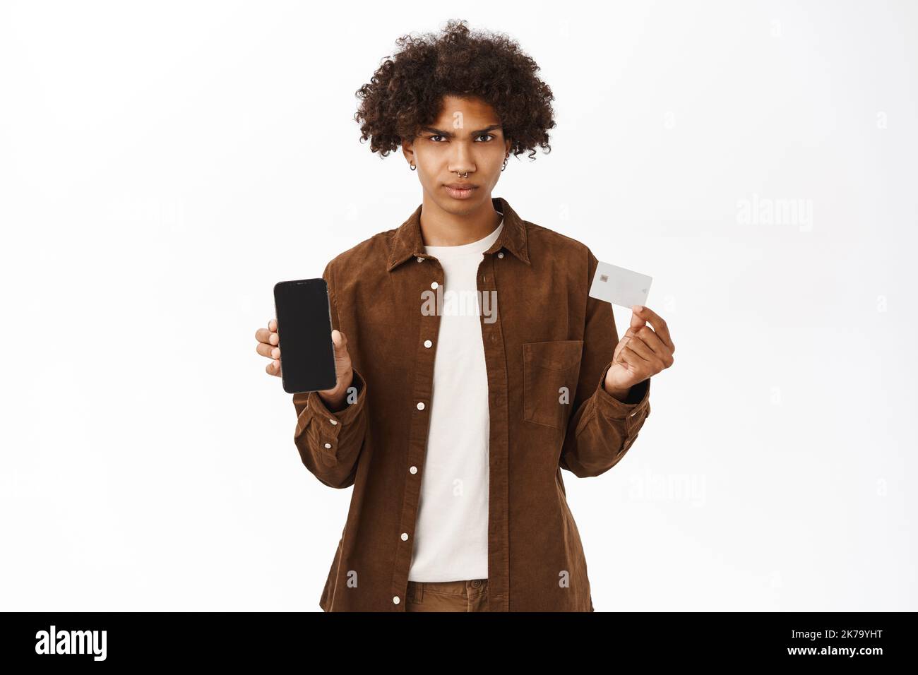 Portrait d'un homme hispanique choqué montre carte de crédit et téléphone mobile, application écran, debout dans des vêtements décontractés sur fond blanc Banque D'Images