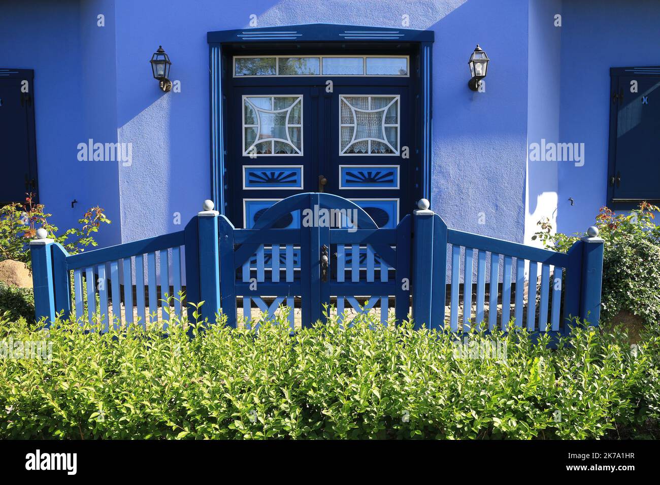 Façade bleue d'une maison moderne avec porte d'entrée derrière une clôture en bois et une haie verte Banque D'Images