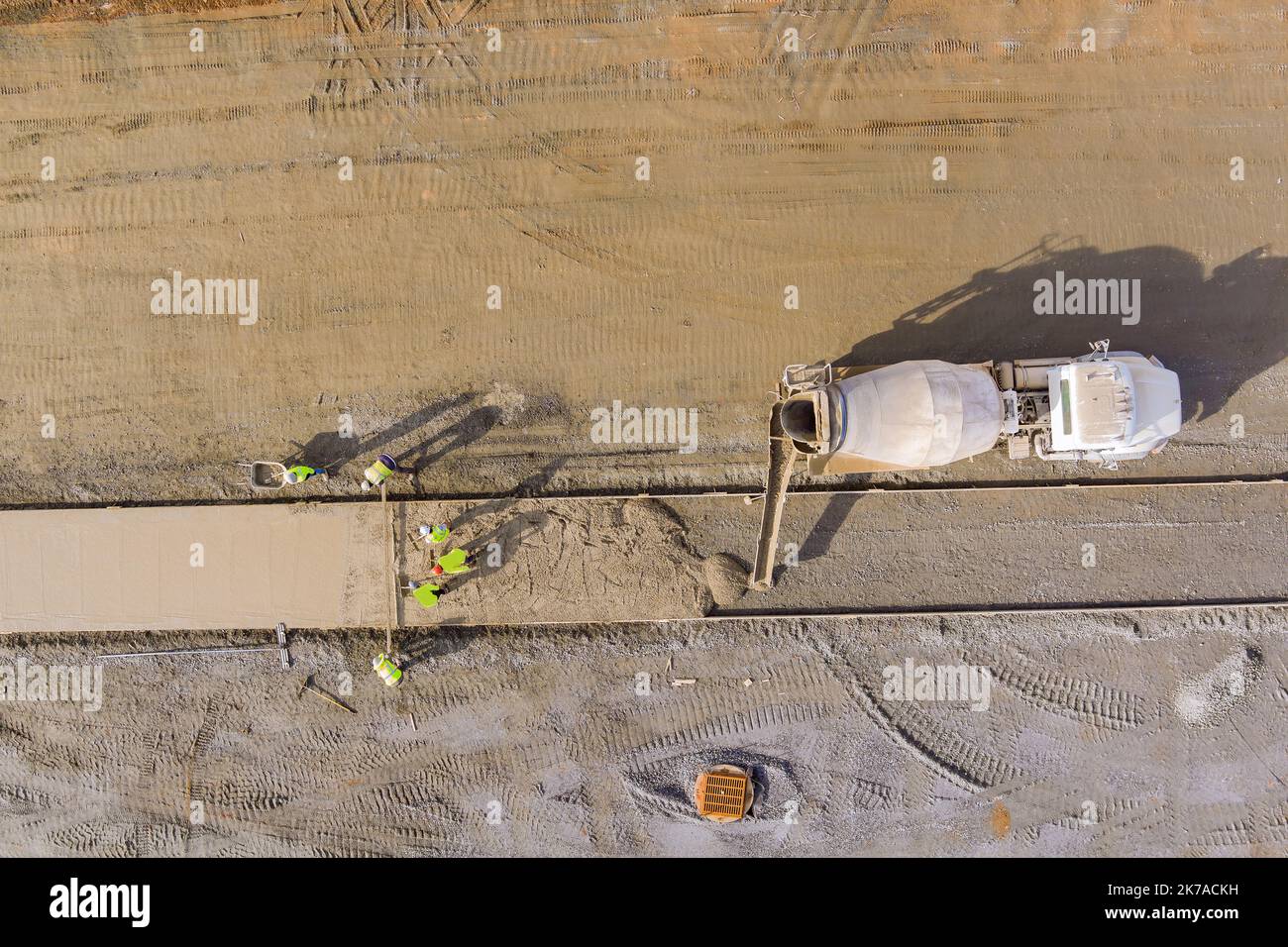 Un camion de mélange de béton versant du béton sur le chantier de construction pendant que les travailleurs versent du ciment pour le trottoir Banque D'Images