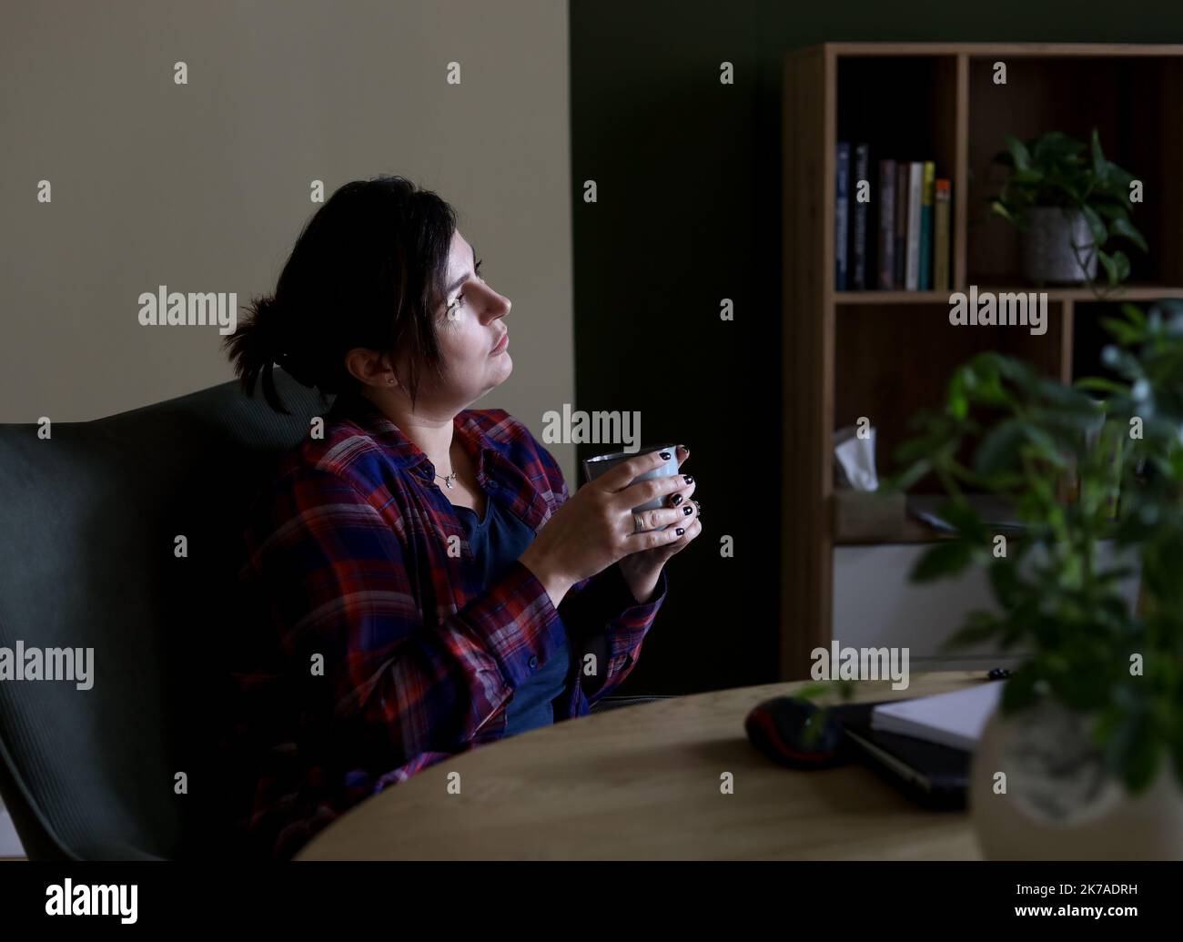 Tranquille, silencieuse, dépressive noire cheveux mûrs femme buvant du thé et regardant la fenêtre dans le salon sombre. Frustration Banque D'Images