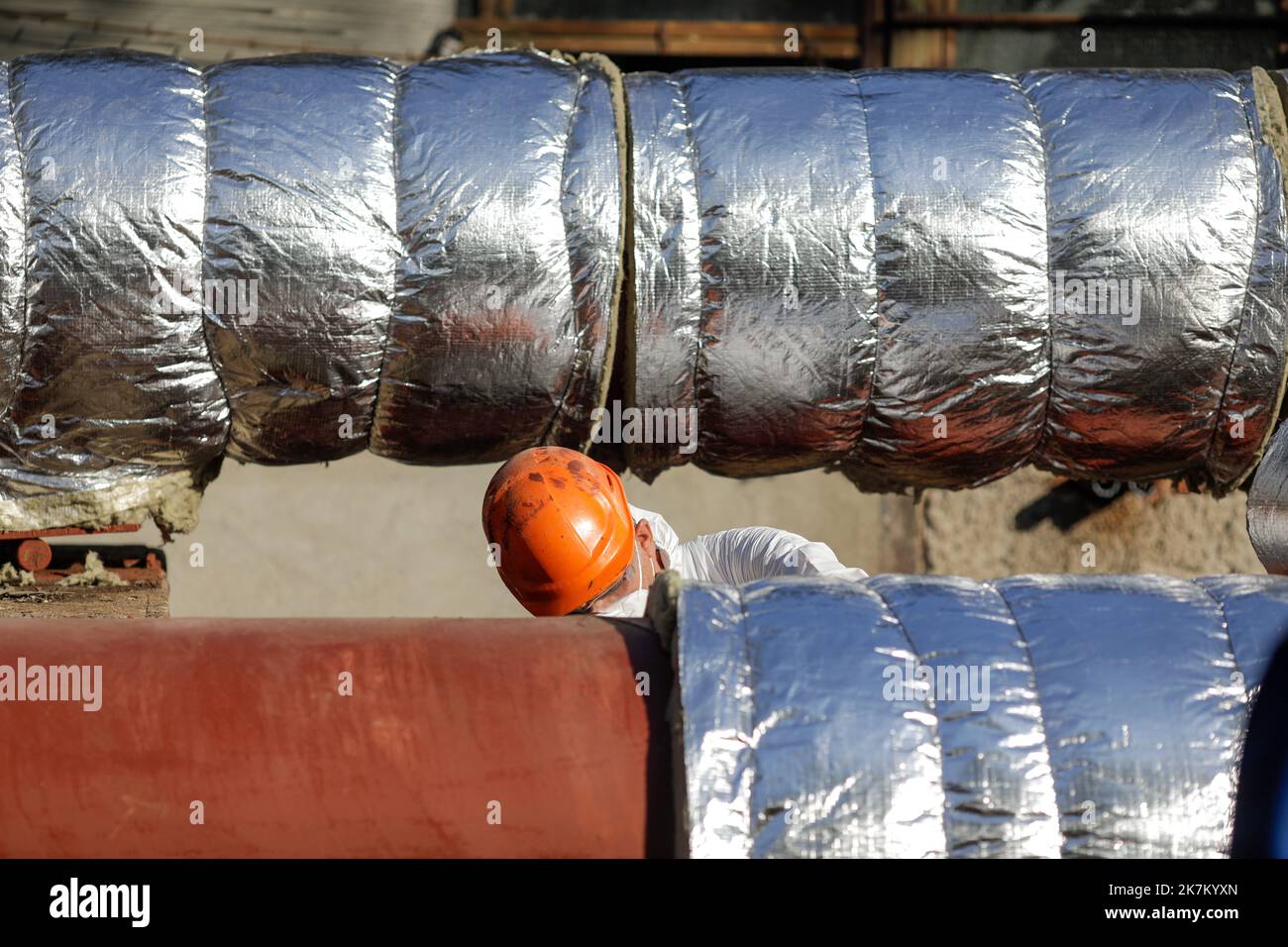 Bucarest, Roumanie - 13 octobre 2022: L'ouvrier utilise la laine de verre pour isoler thermique un pipeline métallique d'eau chaude. Banque D'Images