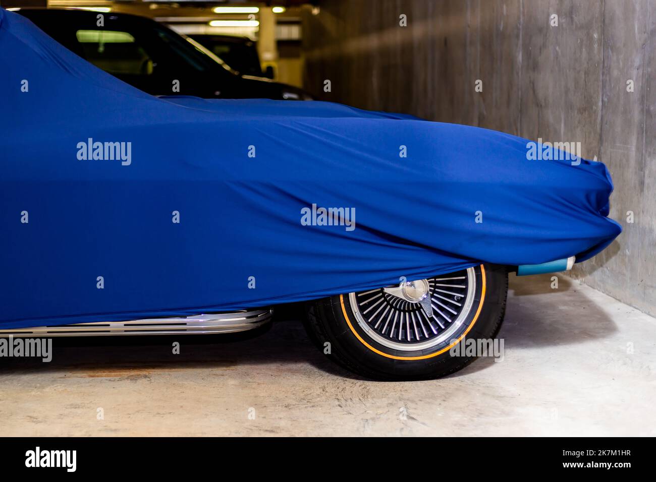 Une voiture de sport classique américaine couverte d'un tissu protecteur attendant dans un garage pour être conduit par le propriétaire.juste un indice de ce qui est en dessous.Une Chevrolet? Banque D'Images