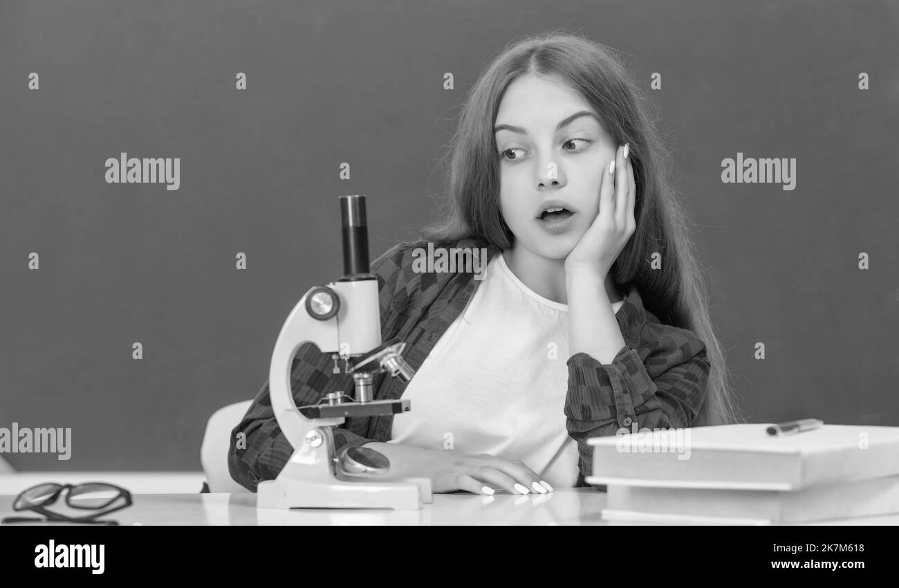 une jeune fille émerveillement en utilisant un microscope à l'école secondaire au tableau noir, biologie Banque D'Images
