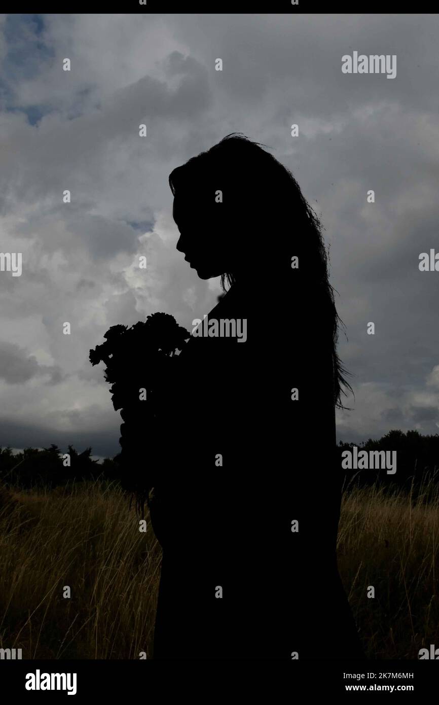Silhouette noire d'une jeune femme contre un ciel sombre nuageux, idée de couverture de livre, Banque D'Images