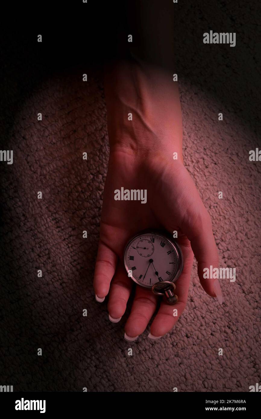 les femmes ont une main ouverte tenant une montre de poche posée sur un sol recouvert de moquette, le style de couverture de livre de thriller mystère. Banque D'Images