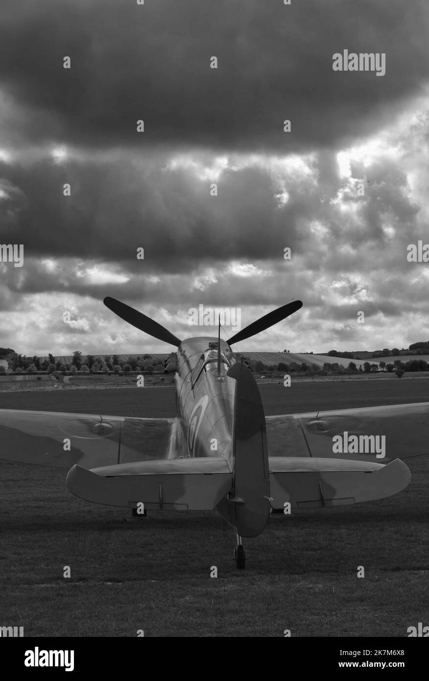une image en noir et blanc en format portrait d'un spitfire garé sur de l'herbe avec des nuages sombres dans le ciel, convient à la couverture de livre Banque D'Images