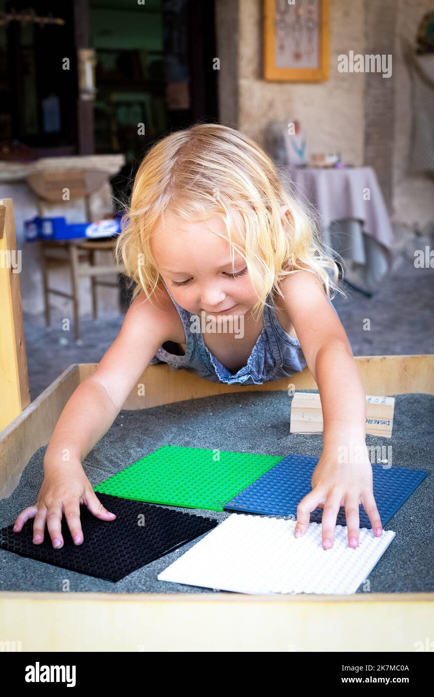 La petite fille blonde joue avec des tables carrées colorées. L'enfant relie des pièces de puzzle. Jeux créatifs pour les enfants de la maternelle. Moteur de développement fin Banque D'Images