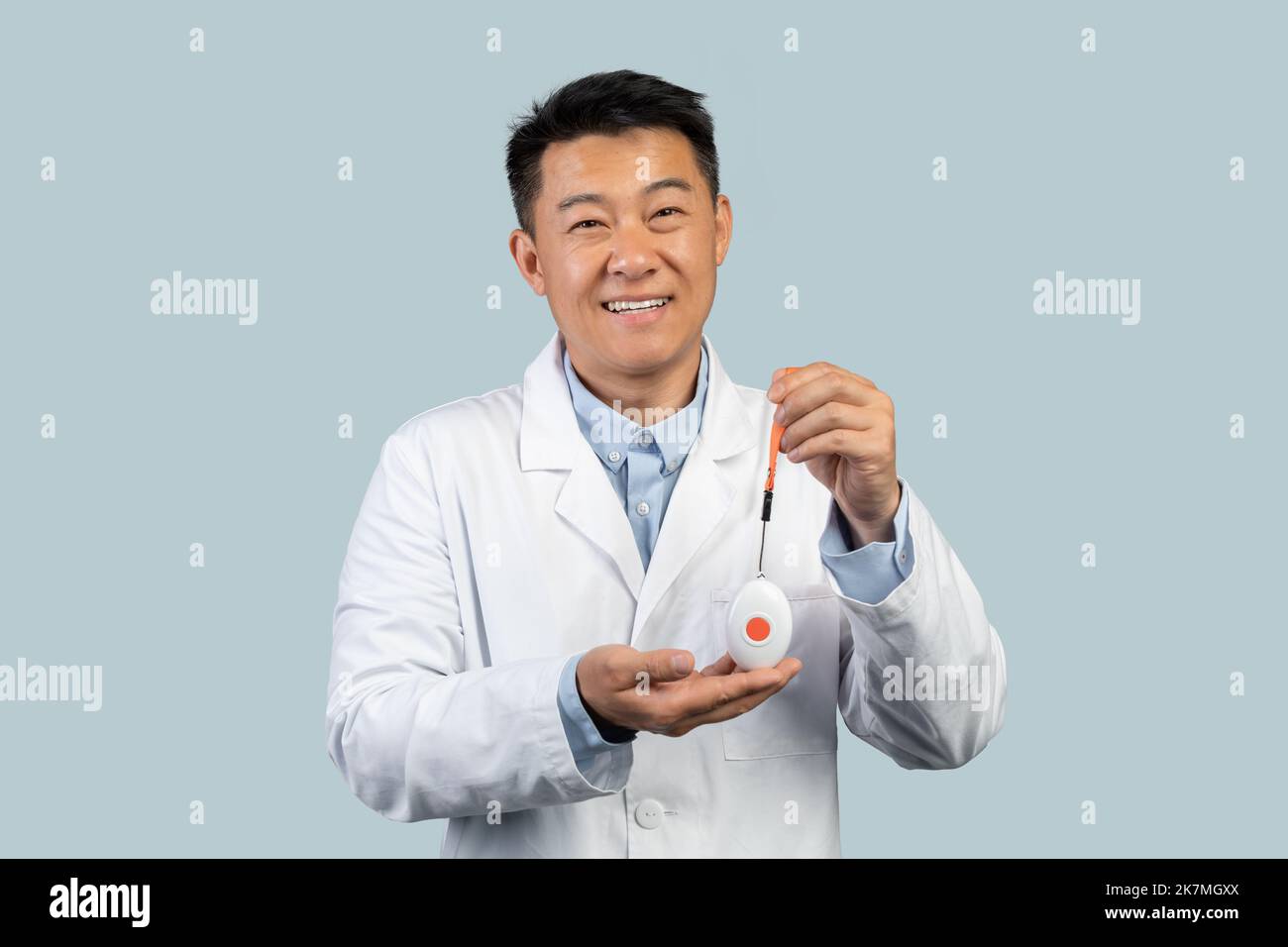 Joyeux médecin chinois d'âge moyen en manteau blanc montrant le bouton d'alarme d'urgence Banque D'Images