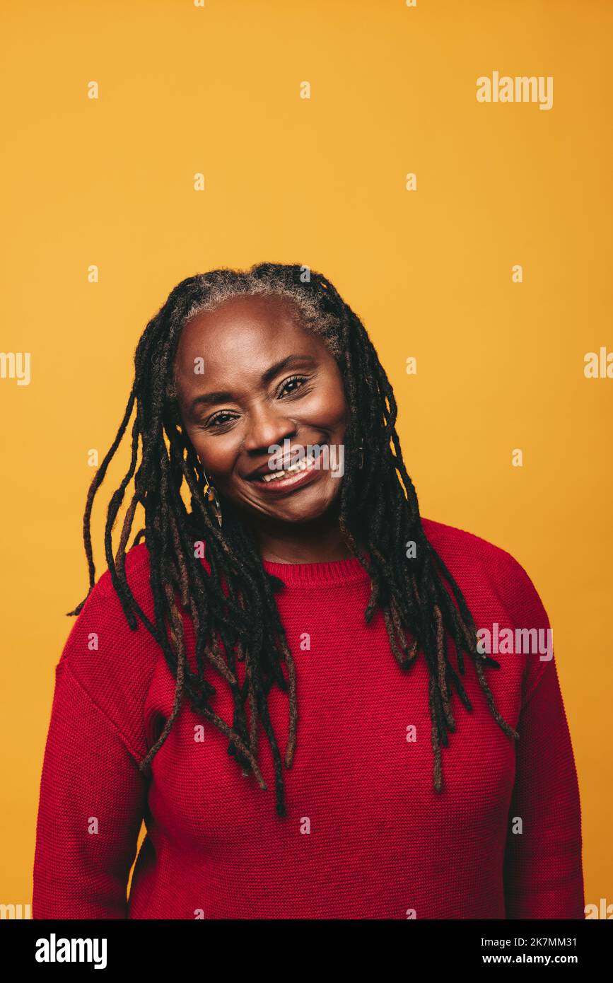 Portrait d'une femme mûre avec des dreadlocks souriant à l'appareil photo tout en se tenant contre un arrière-plan de studio. Femme noire joyeuse embrassant son natura Banque D'Images