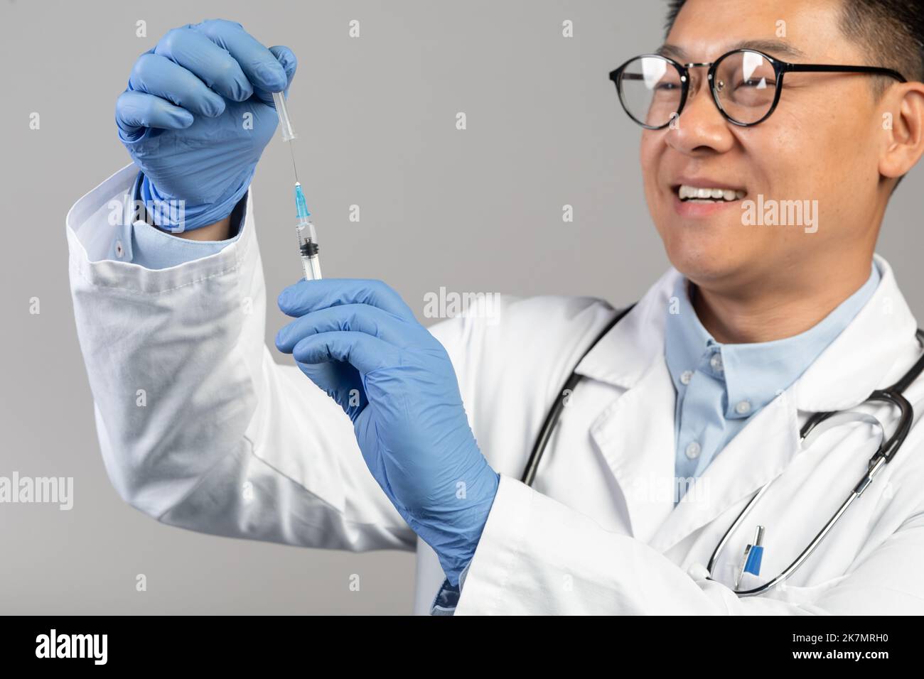 Un médecin chinois souriant d'âge moyen, en manteau blanc et en lunettes, prend le vaccin dans une seringue Banque D'Images