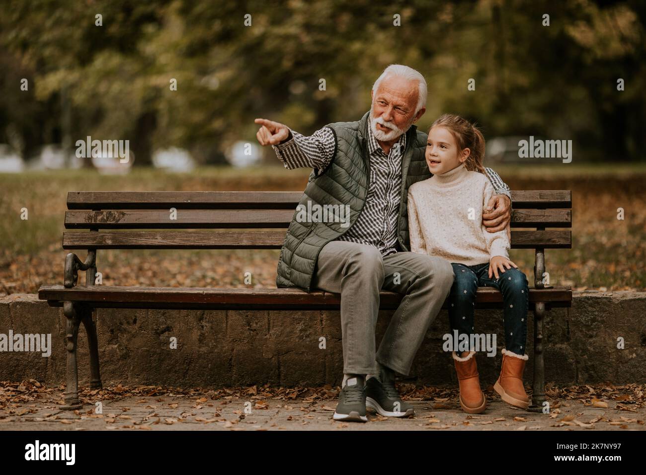 Beau grand-père passant du temps avec sa petite-fille sur banc dans le parc le jour de l'automne Banque D'Images