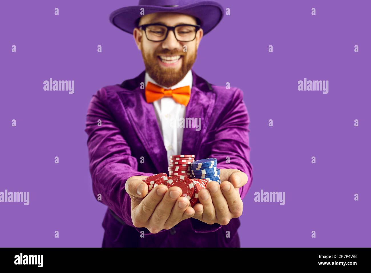 Gros plan des jetons de poker entre les mains d'un homme joyeux et satisfait isolé sur fond violet. Banque D'Images