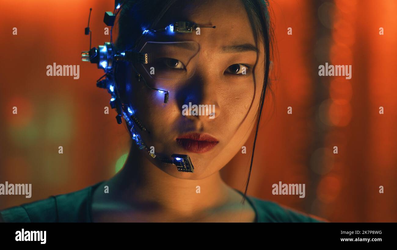 Une fille asiatique de style Cyberpunk avec un casque et un microphone avec de petites lumières LED blanches regarde la caméra. Expressions du visage intenses. Fond SCI-fi avec lumières néon. Banque D'Images