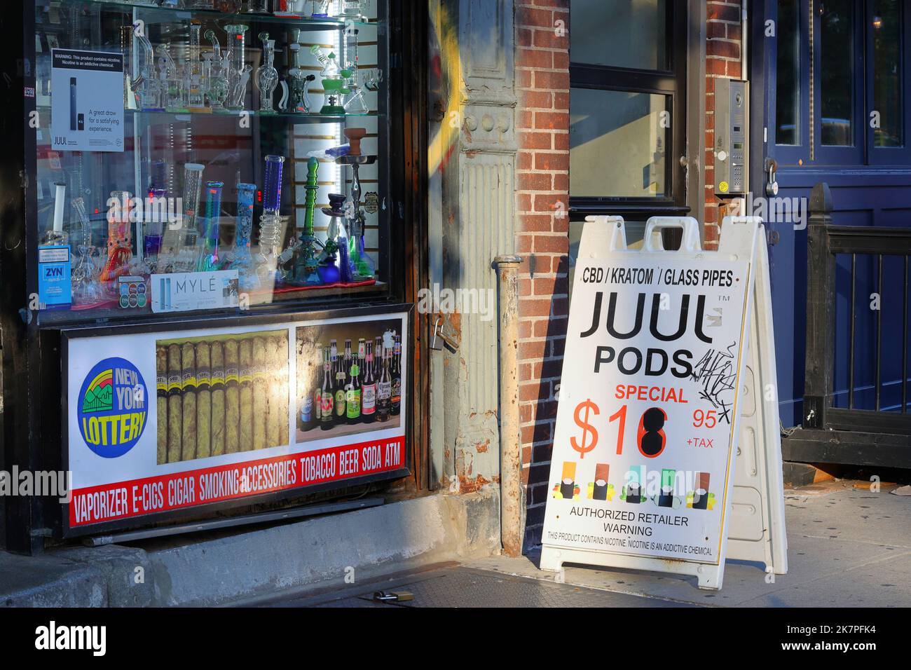 Un magasin de fumée de New York avec des tuyaux d'eau dans la vitrine et des publicités pour les gousses Juul, les vapes, les billets de loterie et la bière. Banque D'Images