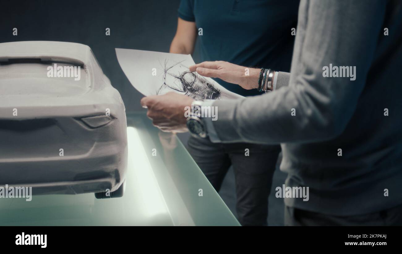 Des concepteurs et des développeurs de voitures expérimentés discutent de la conception de la voiture tout en se tenant face à la sculpture de la voiture prototype. En utilisant les croquis au crayon dans une entreprise de fabrication de voiture de haute technologie. Banque D'Images